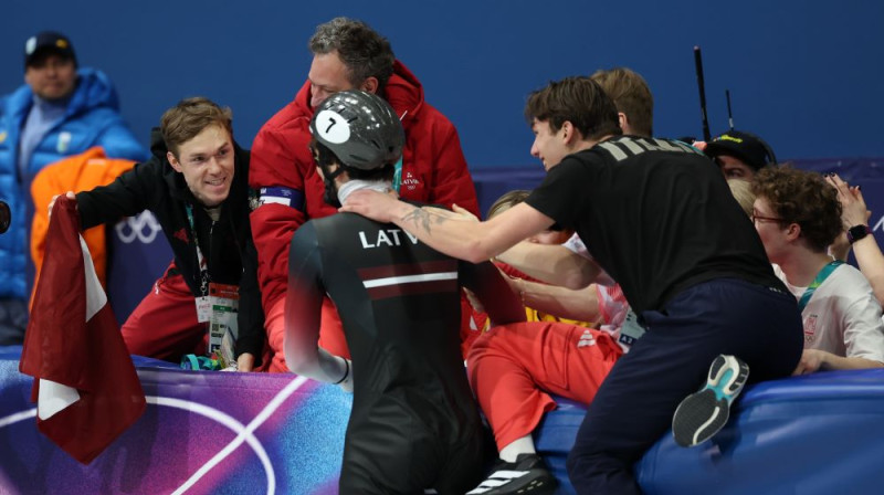 Reinis Bērziņš (pa kreisi) sagaida Robertu Krūzbergu finišā ar Latvijas karogu. Foto: Romāns Kokšarovs/LOK